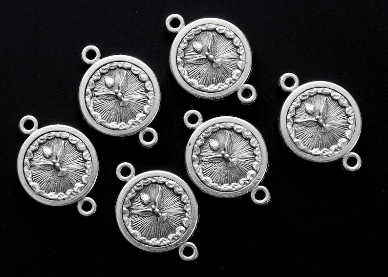 May include: Six silver-toned round charms with a dove and sunburst design. Each charm has two small loops for attaching to other components. The charms are on a black background.