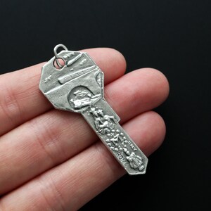 May include: Silver key charm with a detailed design of a bridge and people walking on it. The charm has the words "Rome" and "Italy" inscribed on it.