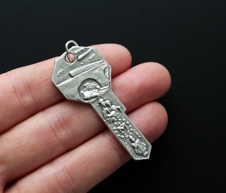 May include: Silver key charm with a detailed design of a bridge and people walking on it. The charm has the words "Rome" and "Italy" inscribed on it.