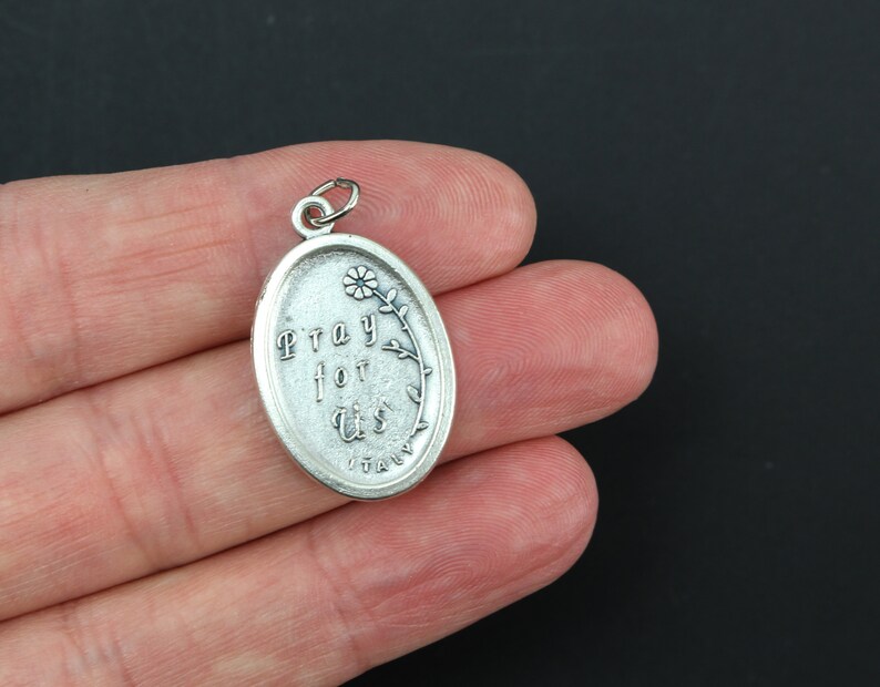 May include: Silver oval charm with the words "Pray for Us" and a small flower design. The charm is made in Italy.