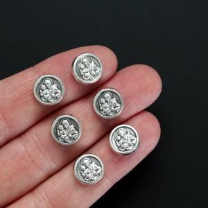 May include: Seven silver-toned round charms with a raised image of a family of three. The charms are on a hand.