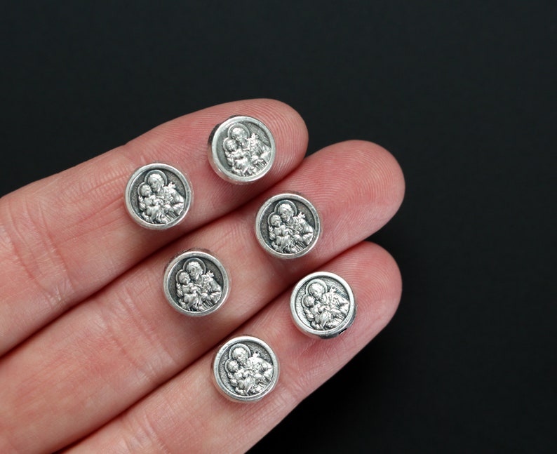 May include: Seven silver-toned round charms with a raised image of a family of three. The charms are on a hand.
