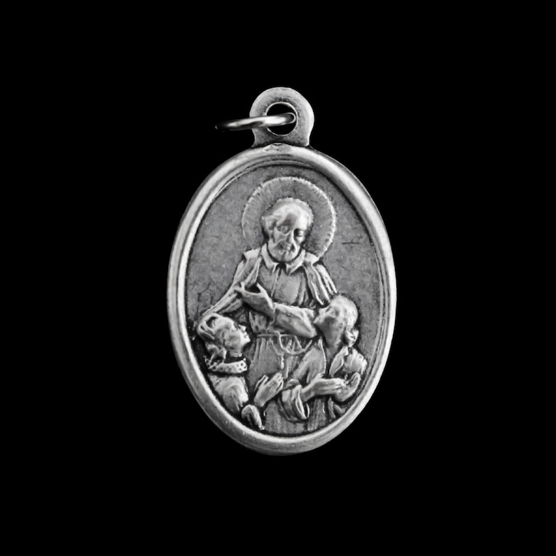 May include: Silver oval pendant featuring a religious image of a man with two children. The man is wearing a robe and has a halo above his head. The children are holding onto the man's robe.