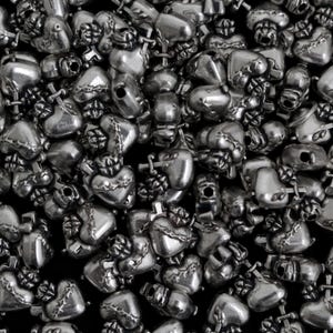 May include: A close-up shot of a pile of silver-colored heart-shaped beads. Each bead has a detailed design, including a cross and a crown. The beads are scattered, creating a textured surface.