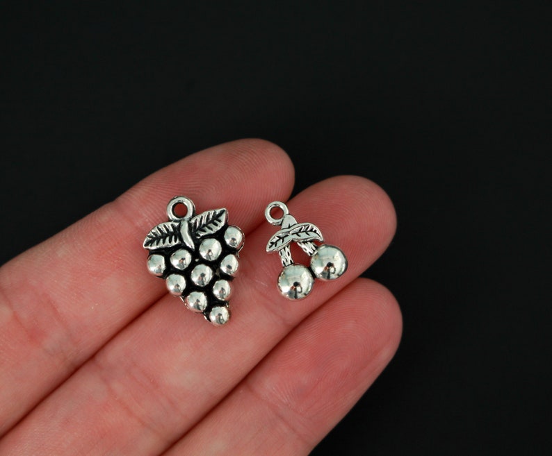 Puede incluir: Dos colgantes de plata, uno con forma de racimo de uvas y el otro con forma de dos cerezas.