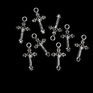 May include: A collection of eight silver-toned metal crucifix charms, each featuring a detailed figure of a person on a cross with an attached circular jump ring at the top. The charms have an oxidized finish that highlights the intricate design.