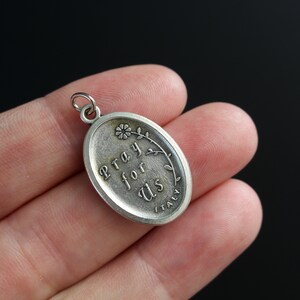 Op de afbeelding: Zilveren ovale bedel met de woorden "Pray for Us" en een klein bloemetjesontwerp. De bedel is gemaakt in Itali&euml;.