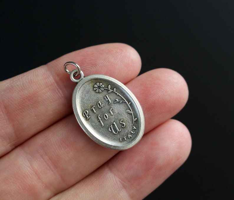 Op de afbeelding: Zilveren ovale bedel met de woorden "Pray for Us" en een klein bloemetjesontwerp. De bedel is gemaakt in Itali&euml;.