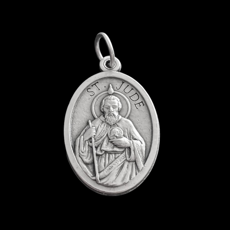 Op de afbeelding: Zilveren ovaalvormige hanger met een afbeelding van de Heilige Judas Thaddeus. De hanger heeft de woorden "ST. JUDE" en een halo rond het hoofd van de heilige.