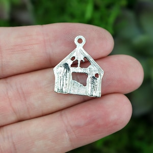 May include: Silver charm shaped like a dog house with a paw print cut out. The charm has a loop at the top for attaching to a necklace or bracelet.