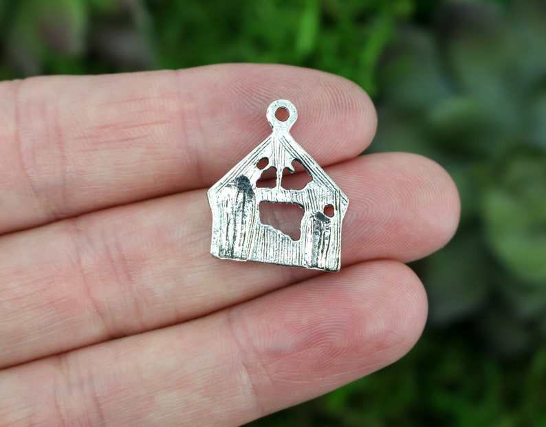 May include: Silver charm shaped like a dog house with a paw print cut out. The charm has a loop at the top for attaching to a necklace or bracelet.
