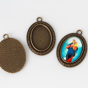 May include: Three oval-shaped metal pendant charms with a bronze finish. Two charms have a textured surface and one charm has a colorful image of a woman holding a child.