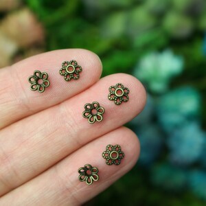 Puede incluir: Cinco tapas de cuentas de metal de color dorado antiguo en forma de flor. Las tapas de cuentas tienen un dise&ntilde;o delicado e intrincado.