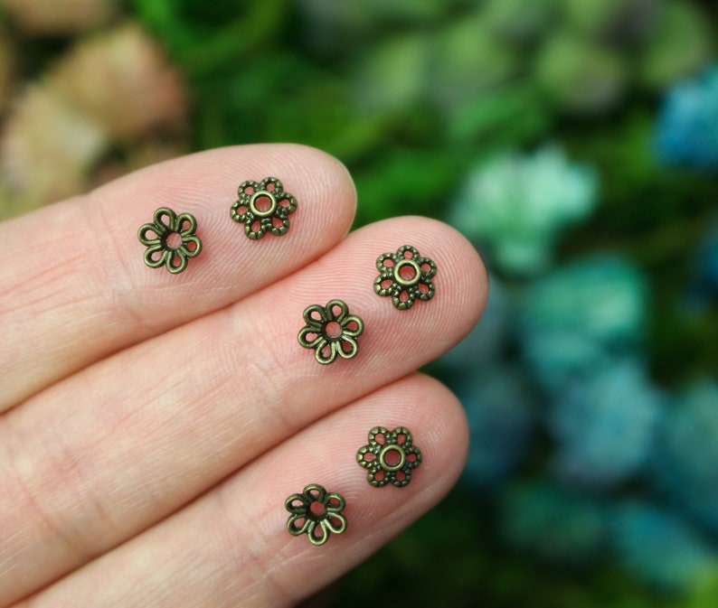 Puede incluir: Cinco tapas de cuentas de metal de color dorado antiguo en forma de flor. Las tapas de cuentas tienen un dise&ntilde;o delicado e intrincado.