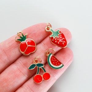 Pu&ograve; includere: Quattro ciondoli dorati con smalto rosso e verde. I ciondoli hanno la forma di una fragola, una fetta di anguria, una ciliegia e un melograno.