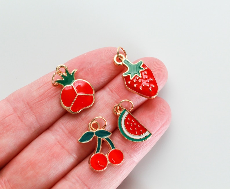 Pu&ograve; includere: Quattro ciondoli dorati con smalto rosso e verde. I ciondoli hanno la forma di una fragola, una fetta di anguria, una ciliegia e un melograno.