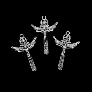 May include: Three silver crucifix pendants, each depicting Jesus Christ with outstretched arms and a halo. The crosses are intricately detailed and set against a black backdrop. The pendants are designed with intricate details.