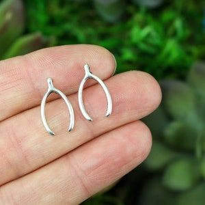 May include: A pair of silver wishbone earrings. The earrings are small and delicate, and they are perfect for adding a touch of whimsy to any outfit.