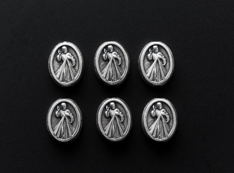 Puede incluir: Seis dijes de metal plateados con una imagen religiosa de un hombre con los brazos extendidos. Los dijes est&aacute;n dispuestos en dos filas de tres sobre un fondo negro.