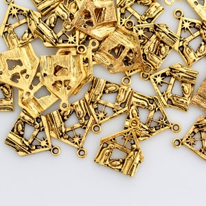 May include: A pile of gold-colored metal charms shaped like a nativity scene. Each charm features a detailed design of a stable with a star on top and figures inside.