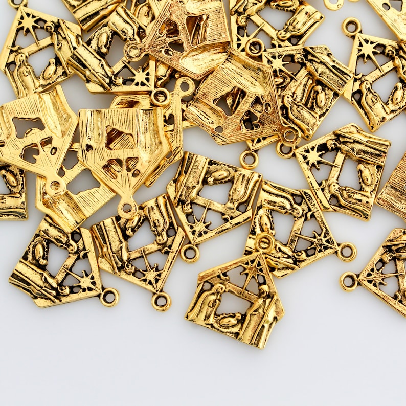 May include: A pile of gold-colored metal charms shaped like a nativity scene. Each charm features a detailed design of a stable with a star on top and figures inside.