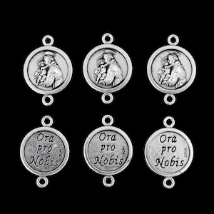 May include: Six silver-toned metal charms featuring a religious image of Saint Anthony of Padua holding a baby on one side and the words "Ora pro Nobis" on the other side.