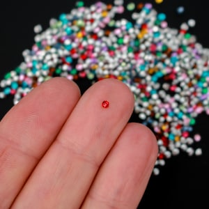 May include: A single red rhinestone on a fingertip against a background of colorful rhinestones.