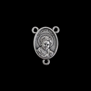 May include: A silver oval pendant depicting St. Carlo Acutis. The pendant has three loops for attachment. The text "St. Carlo Acutis" is inscribed around the portrait of the saint.