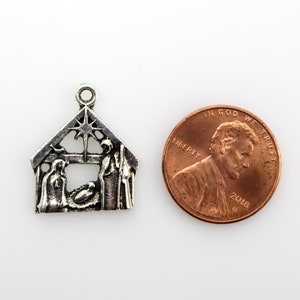 May include: Silver charm depicting the nativity scene with Mary, Joseph, and baby Jesus in a manger. The charm is shaped like a house with a star on top and is about the size of a UK penny.