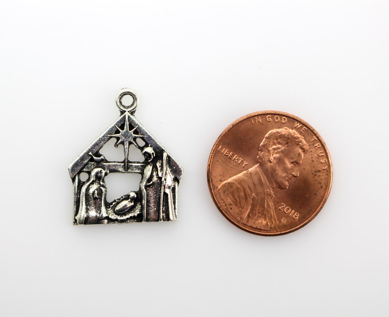 May include: Silver charm depicting the nativity scene with Mary, Joseph, and baby Jesus in a manger. The charm is shaped like a house with a star on top and is about the size of a UK penny.