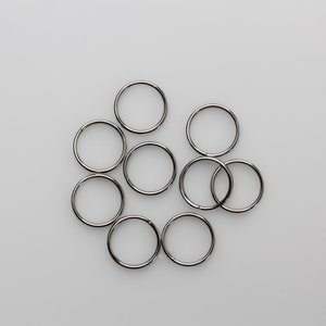 May include: A collection of nine silver-colored metal split rings, arranged in a loose cluster against a plain white background. The rings are circular and appear to be made of a shiny, reflective material.