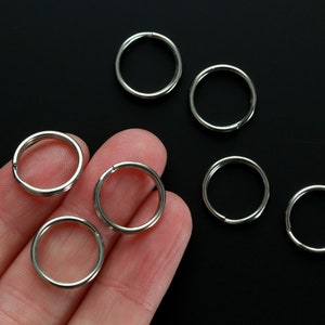 Könnte beinhalten: Eine Sammlung silberfarbener Schlüsselringe mit geteiltem Ring, vor schwarzem Hintergrund. Die Ringe sind kreisförmig, mit einem Spalt zum Anbringen von Schlüsseln oder anderen Gegenständen. Das Bild zeigt mehrere Ringe, einige scharf, andere leicht unscharf.