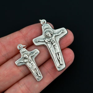 May include: Two silver crucifixes with a raised image of Jesus Christ on the cross. The larger crucifix is about 2 inches tall and the smaller crucifix is about 1 inch tall.
