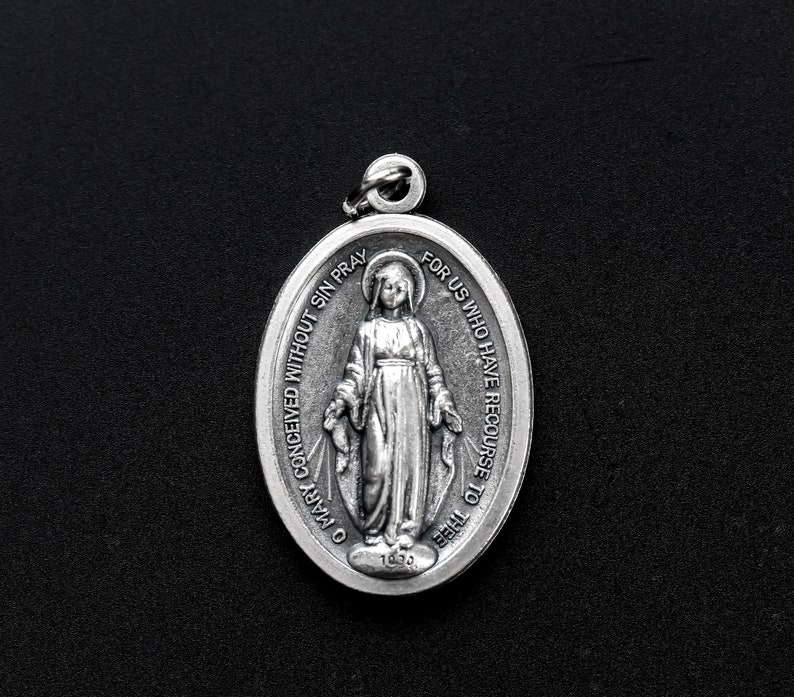 May include: Silver oval pendant with a depiction of the Virgin Mary and the text "O Mary conceived without sin pray for us who have recourse to thee".
