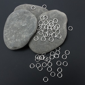 Könnte beinhalten: Ein Haufen silberner Sprungringe auf zwei grauen Steinen. Die Sprungringe sind um die Steine herum verstreut.