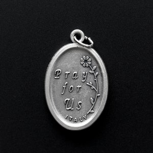 May include: Silver oval charm with the words "Pray for Us" and a small flower design. The charm is made in Italy.