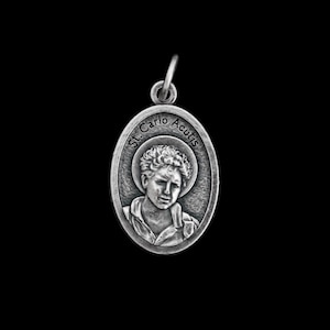 May include: Silver oval pendant with a raised image of a young man with short curly hair. The pendant has the text "St. Carlo Acutis" around the edge.
