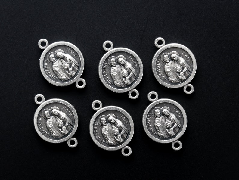 May include: Six silver-toned Holy Family medallions. Each circular pendant features an embossed image of a family and the words "HOLY FAMILY" and "ITALY". The medallions have small loops for attaching to a chain or other jewelry.