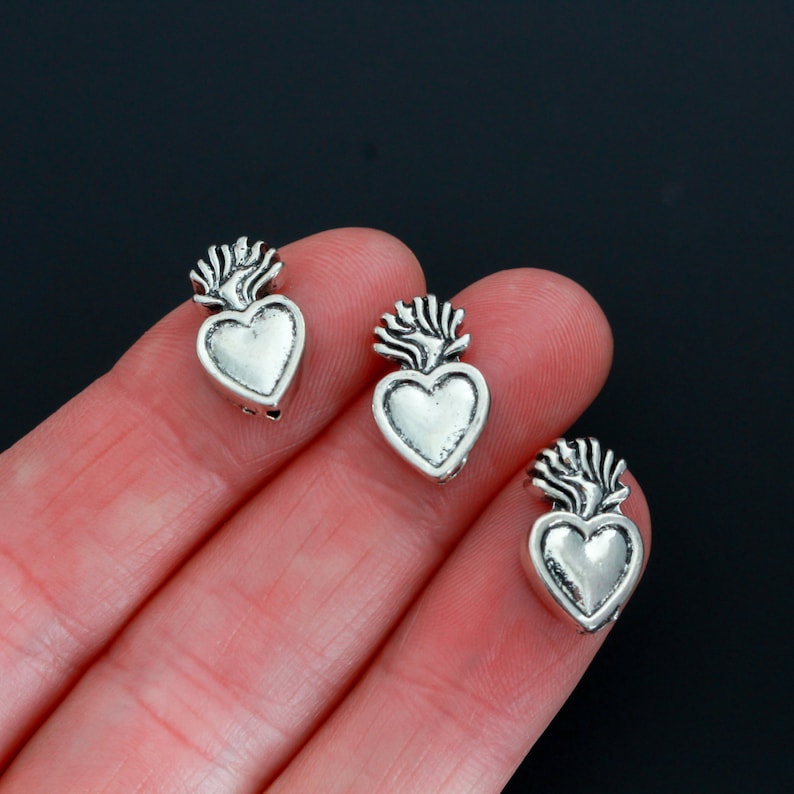 May include: Three silver-toned heart charms with a flame design on top. The charms are small and delicate, and they would be perfect for adding a touch of whimsy to jewelry or crafts.