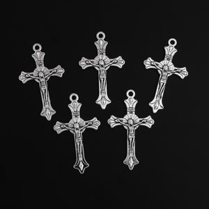 May include: Five silver-toned crucifix pendants with a detailed depiction of Jesus Christ. Each cross features the inscription "INRI" at the top and a loop for hanging. The crosses are arranged against a black background.