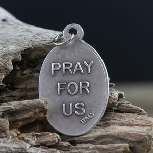 May include: Silver oval charm with the words "Pray For Us" and "Italy" engraved on it.