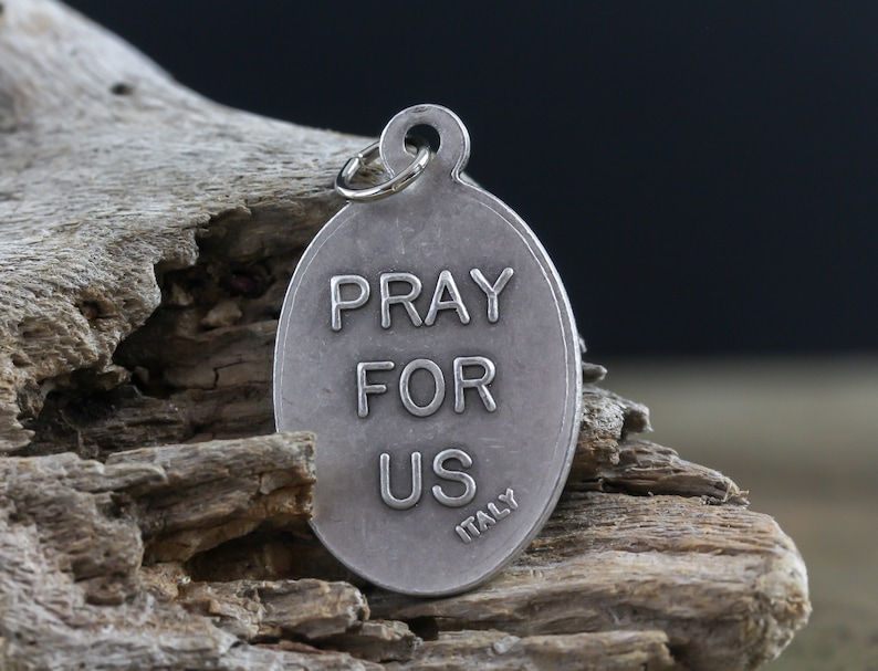 May include: Silver oval charm with the words "Pray For Us" and "Italy" engraved on it.