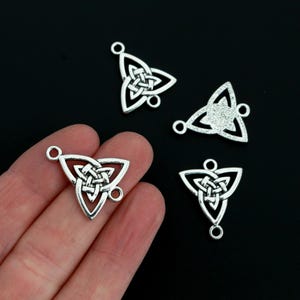 May include: Silver-toned metal Celtic knot charms. The charms are triangular with a detailed interwoven knot design in the center. Each charm has small loops for attaching to jewelry or other crafts. The background is black.