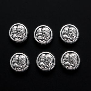 May include: Six silver-toned metal charms featuring an image of two angels embracing. Each charm is round and has a raised design.