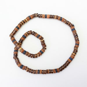 May include: A set of two brown and blue wooden bead necklaces. The larger necklace is longer and has a larger circumference than the smaller necklace.