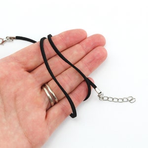 以下が含まれることがあります： 銀色のロブスタークラスプと銀色のチェーンエクステンションが付いた、黒いスエードコードネックレスです。