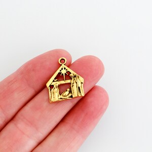 May include: Gold-toned metal charm featuring a nativity scene with a star, a manger, and figures of Mary, Joseph, and a baby Jesus.