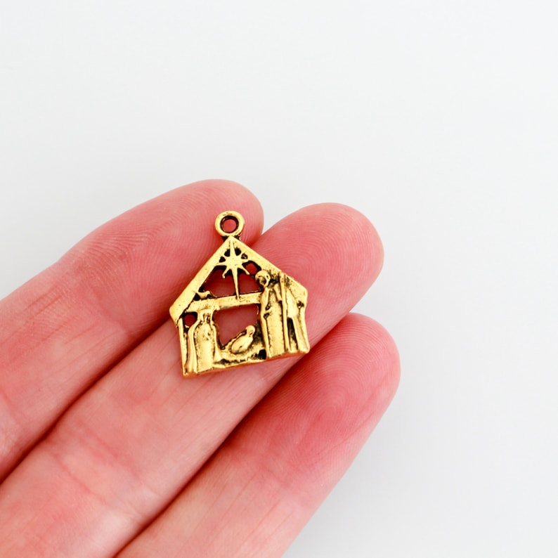 May include: Gold-toned metal charm featuring a nativity scene with a star, a manger, and figures of Mary, Joseph, and a baby Jesus.