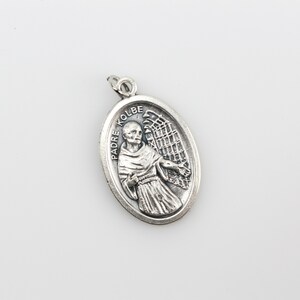 May include: Silver oval pendant with a depiction of Padre Kolbe, a Catholic saint, with an angel's wings behind him. The pendant has the words "Padre Kolbe" inscribed on it.