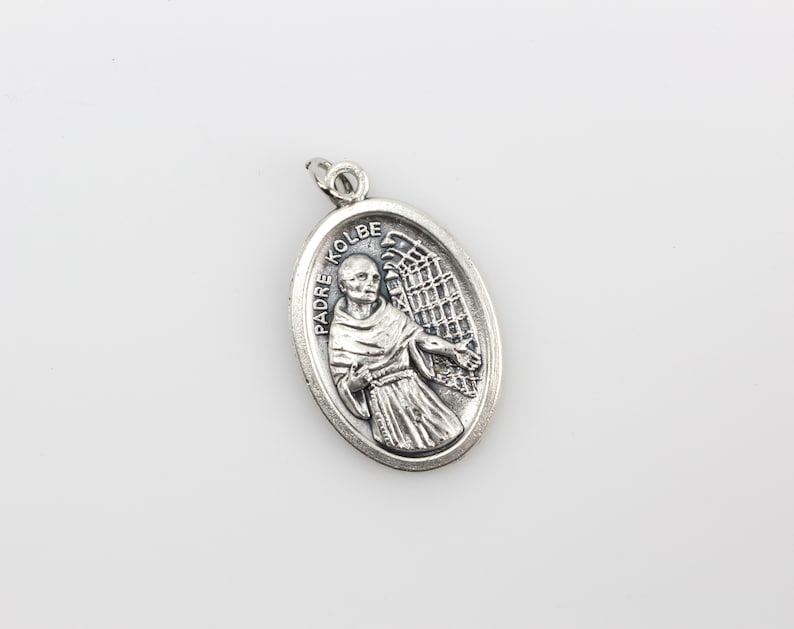 May include: Silver oval pendant with a depiction of Padre Kolbe, a Catholic saint, with an angel's wings behind him. The pendant has the words "Padre Kolbe" inscribed on it.